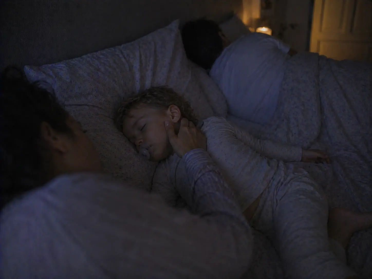 Maminka se v noci v rodinné posteli jemně dotýká tváře spícího dítěte